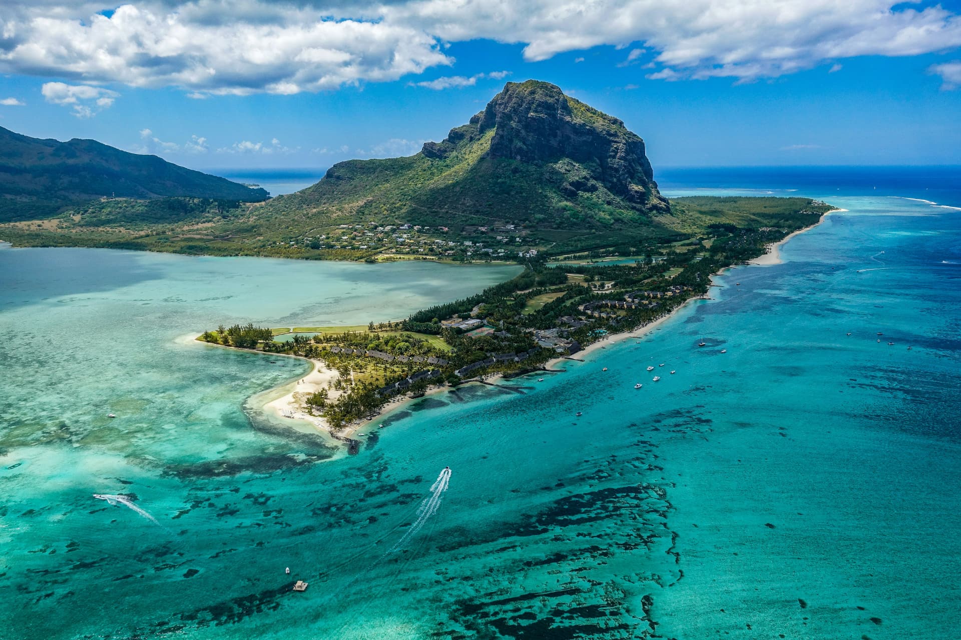 Flygvy över halvön Le Morne med hotellbyggnader, båtar i den turkosa lagunen och det gröna berget bakom