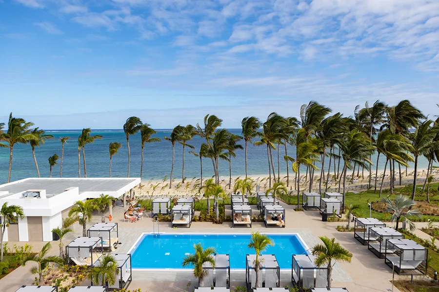Poolområdet på Riu Palace Mauritius med solsängar, palmer och stranden bakom