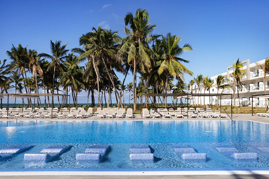 Poolområdet på Riu Turquoise med solsängar i vattnet, palmer och havet i bakgrunden