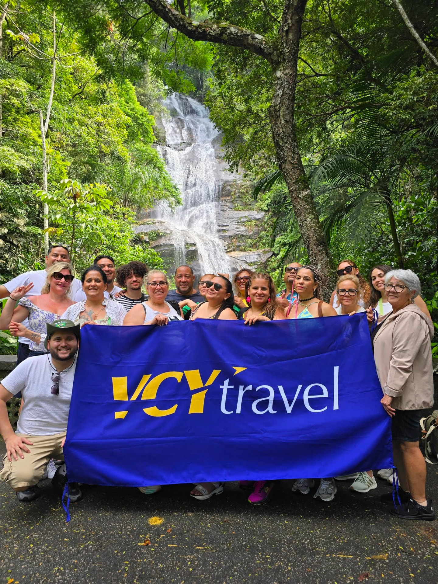 VCY Travels gruppresa till Rio Carneval 2026 – gruppen framför ett vattenfall i Tijuca-skogen med VCY Travel-flaggan